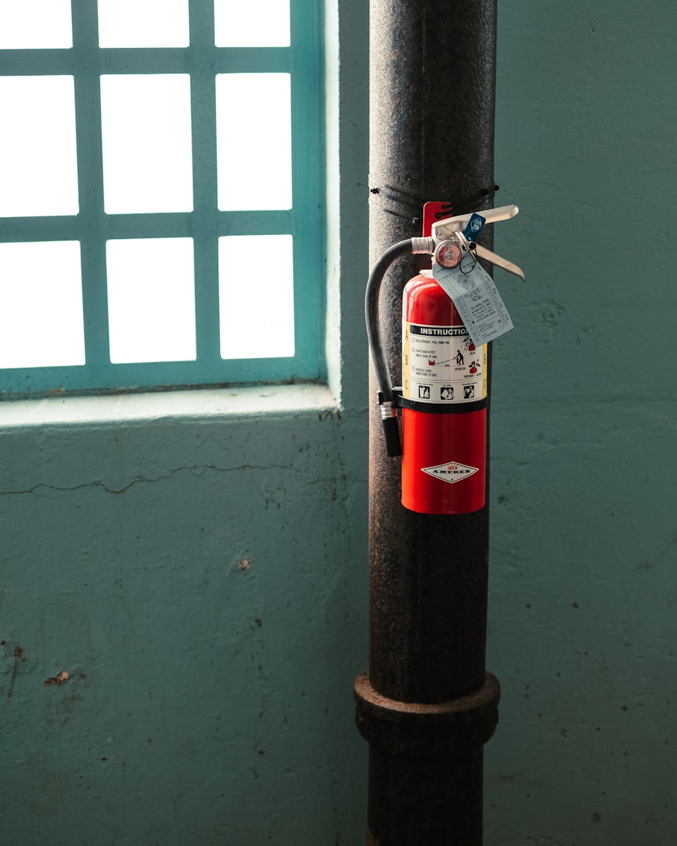red fire extinguisher on brown metal pipe near window